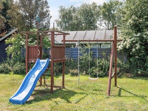 Une aire de jeux avec un toboggan, des balançoires et une structure d’escalade en bois.