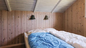Ein Einzelbett mit himmelblauer und weißer Bettdecke in einem Zimmer mit Holzwänden und einer geneigten Decke.