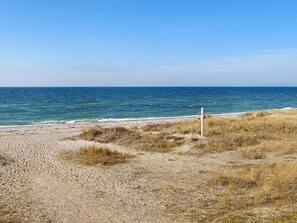 Une plage avec un panneau indiquant la présence d’un sauveteur, un terrain sablonneux et l’océan.