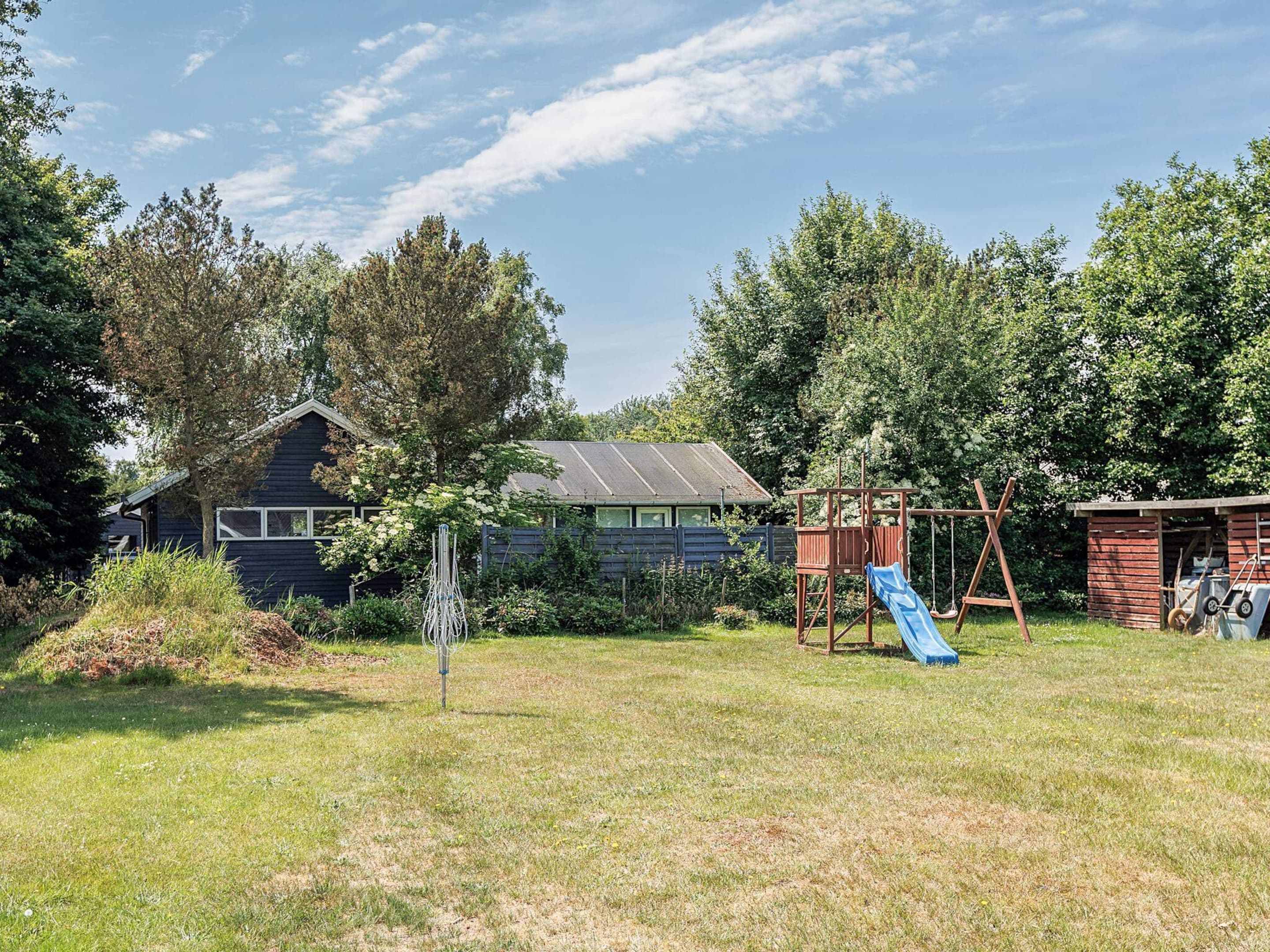 Ein Garten mit einem hölzernen Spielhaus, einer Rutsche und einer Schaukel.