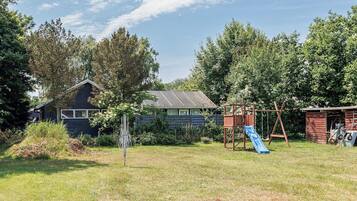 Ein Garten mit einem hölzernen Spielhaus, einer Rutsche und einer Schaukel.