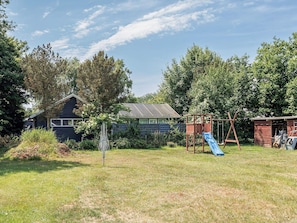 A backyard with a wooden playhouse, a slide, and a swing set.