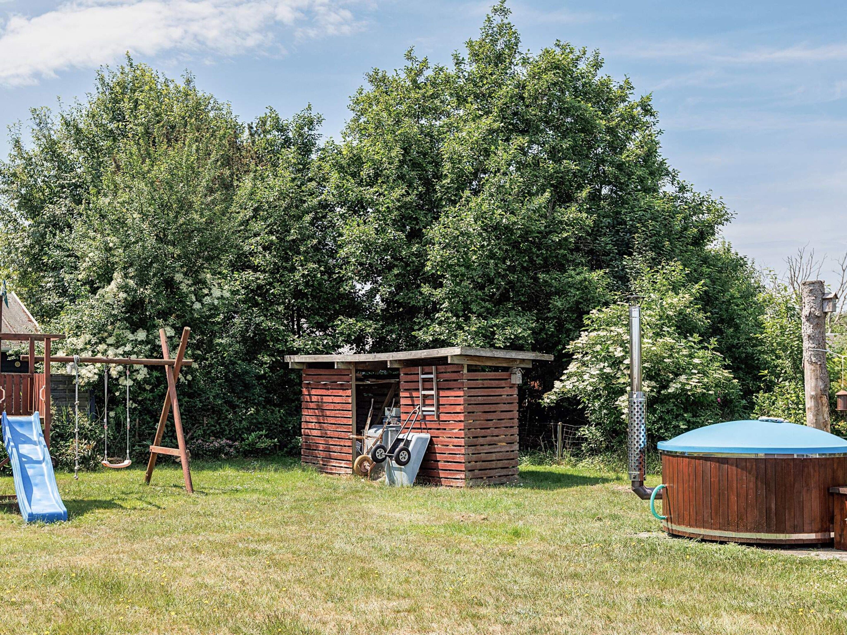 A small wooden cabin with a porch, surrounded by a grassy yard and dense trees.