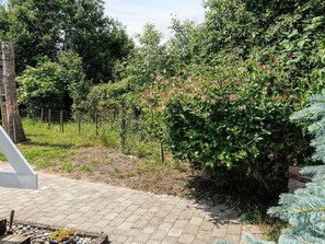 A paved pathway leading through a garden with dense foliage and a birdhouse on a tree. - 5 Star Holiday Home in Dannemare (Dannemare)