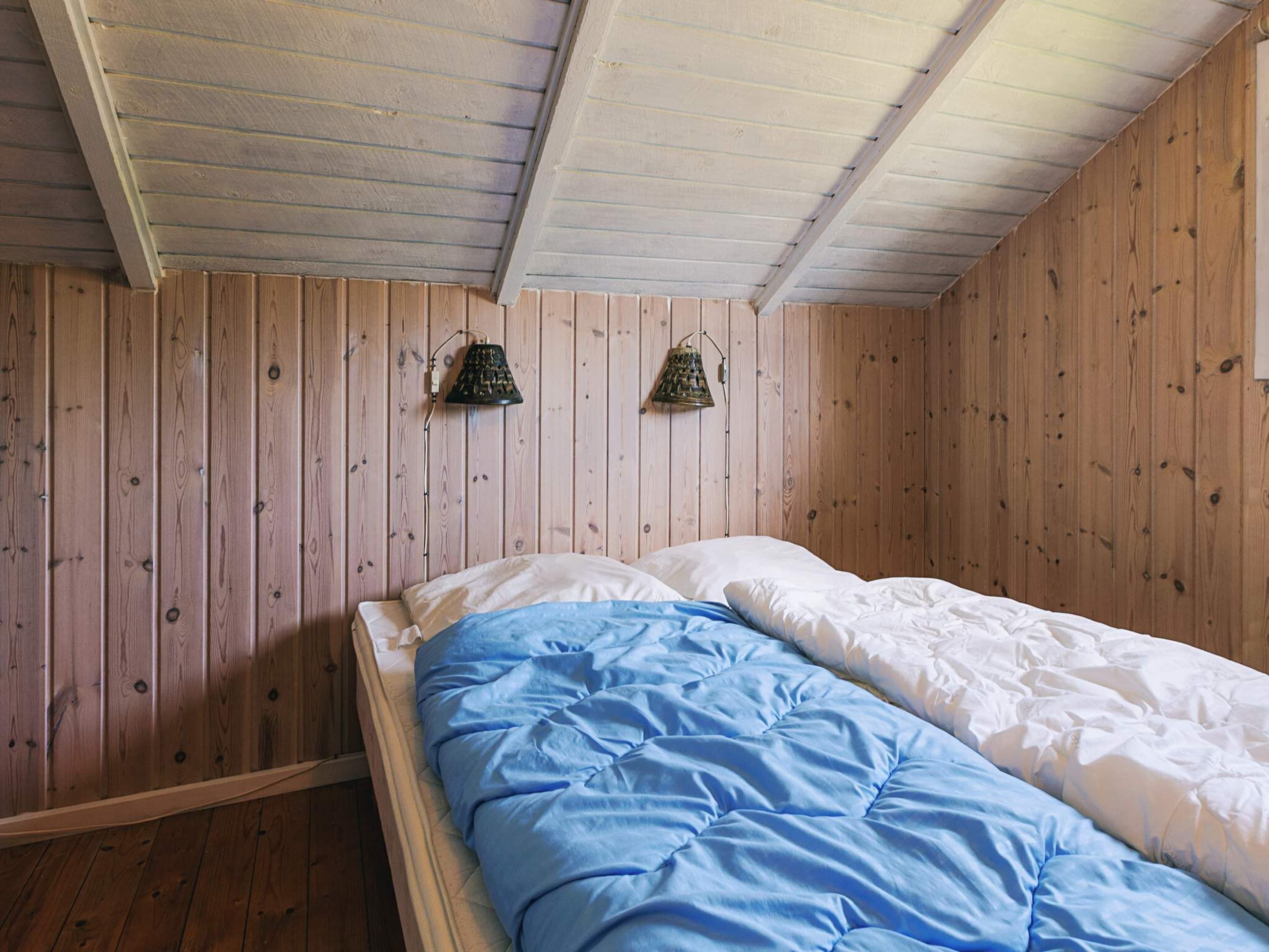 A single bed with a blue and white duvet in a room with wooden walls and a sloped ceiling.