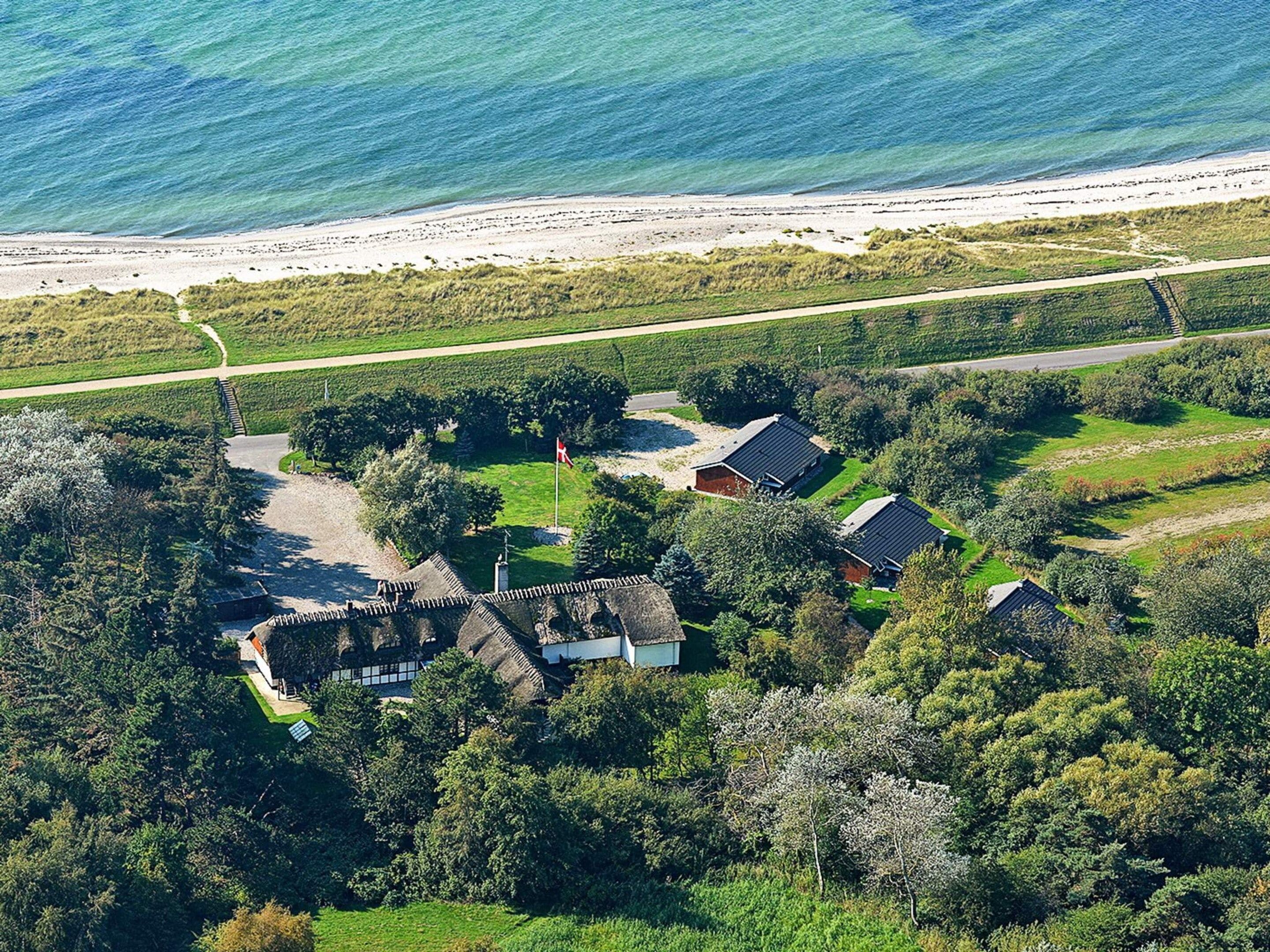 Propiedad costera con vista a la playa, camino de entrada pavimentado y una combinación de edificaciones residenciales y vegetación.