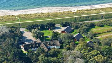 A coastal property with a beach view, a paved driveway, and a mix of residential buildings and greenery.