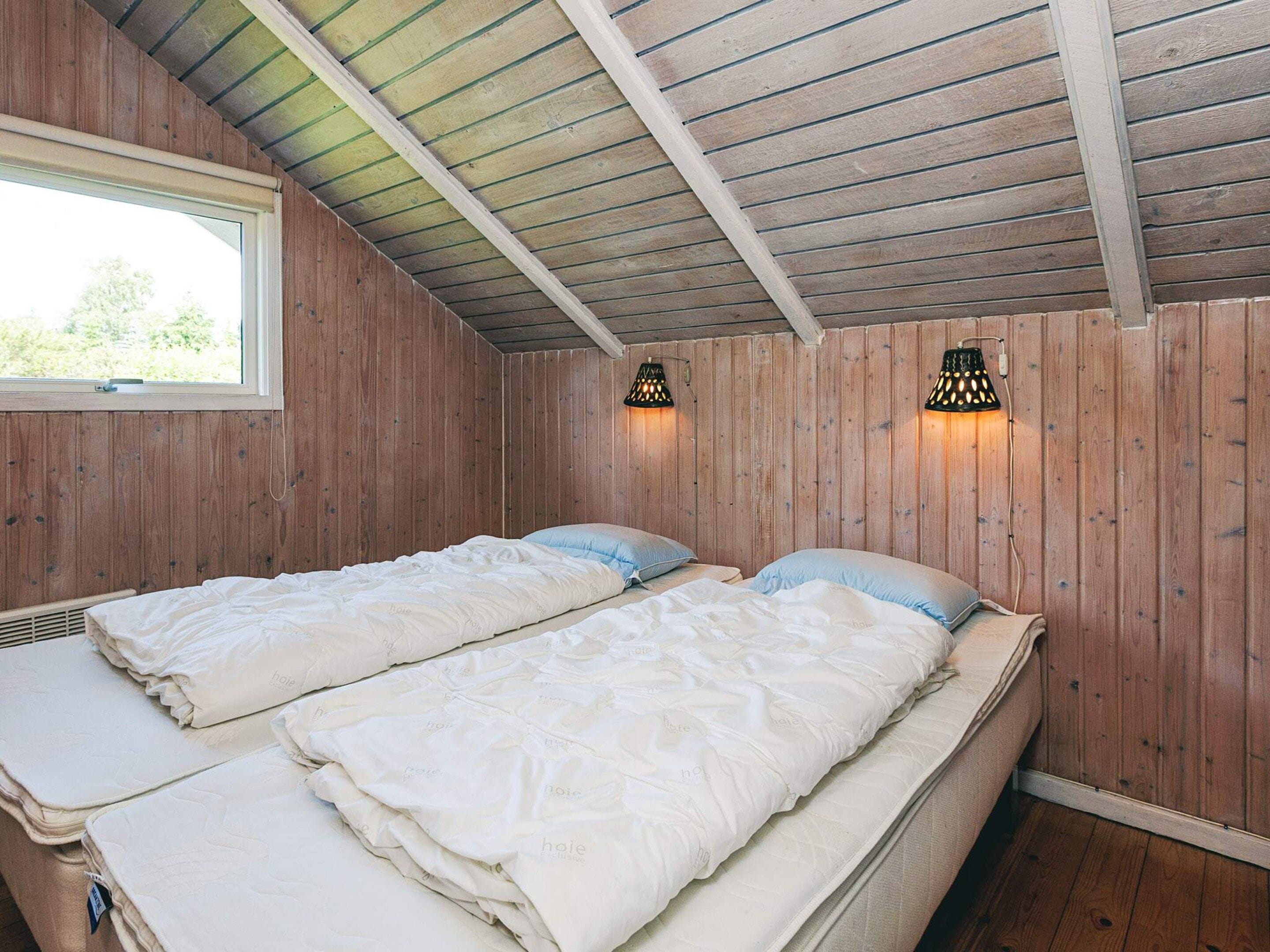 Una habitación con dos camas, paredes de madera, techo inclinado y dos lámparas fijadas a la pared.