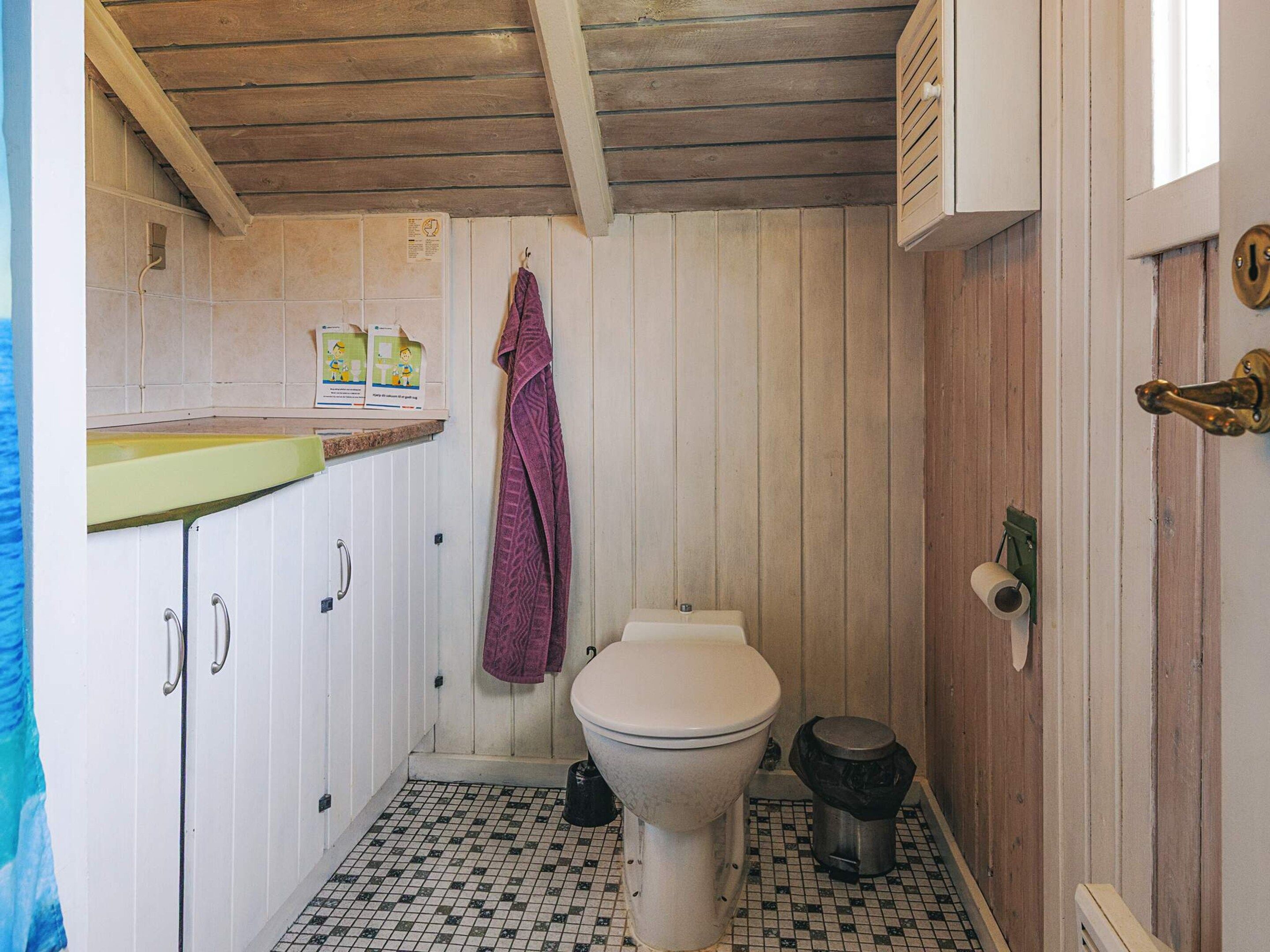 A small bathroom with a toilet, a trash bin, a towel hanging on the wall, and a shower area.