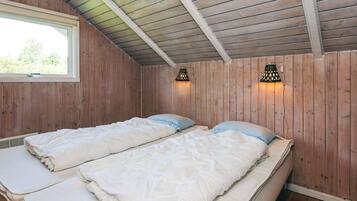 Ein Zimmer mit zwei Betten, Holzwänden, einer schrägen Decke und zwei Wandlampen.