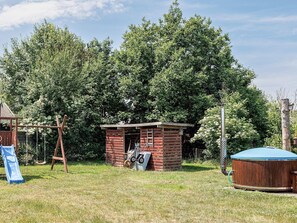 A small wooden structure with a ladder, a swing set, and a hot tub in a grassy yard with dense trees in the background. - 5 Star Holiday Home in Dannemare (Dannemare)
