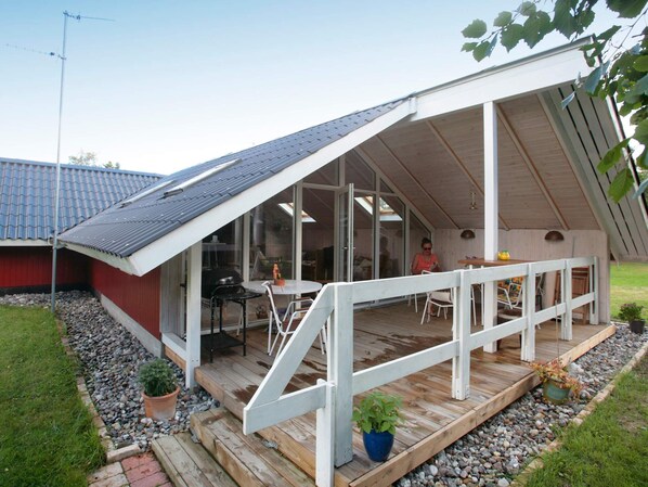 A modern house with a sloped roof, a covered patio with a wooden deck, and a glass door leading to an interior space.
