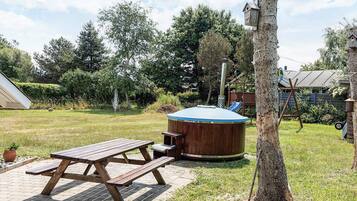 Ein Holztisch für Picknicks und ein Whirlpool in einem Garten mit Bäumen und einer Spielanlage im Hintergrund.