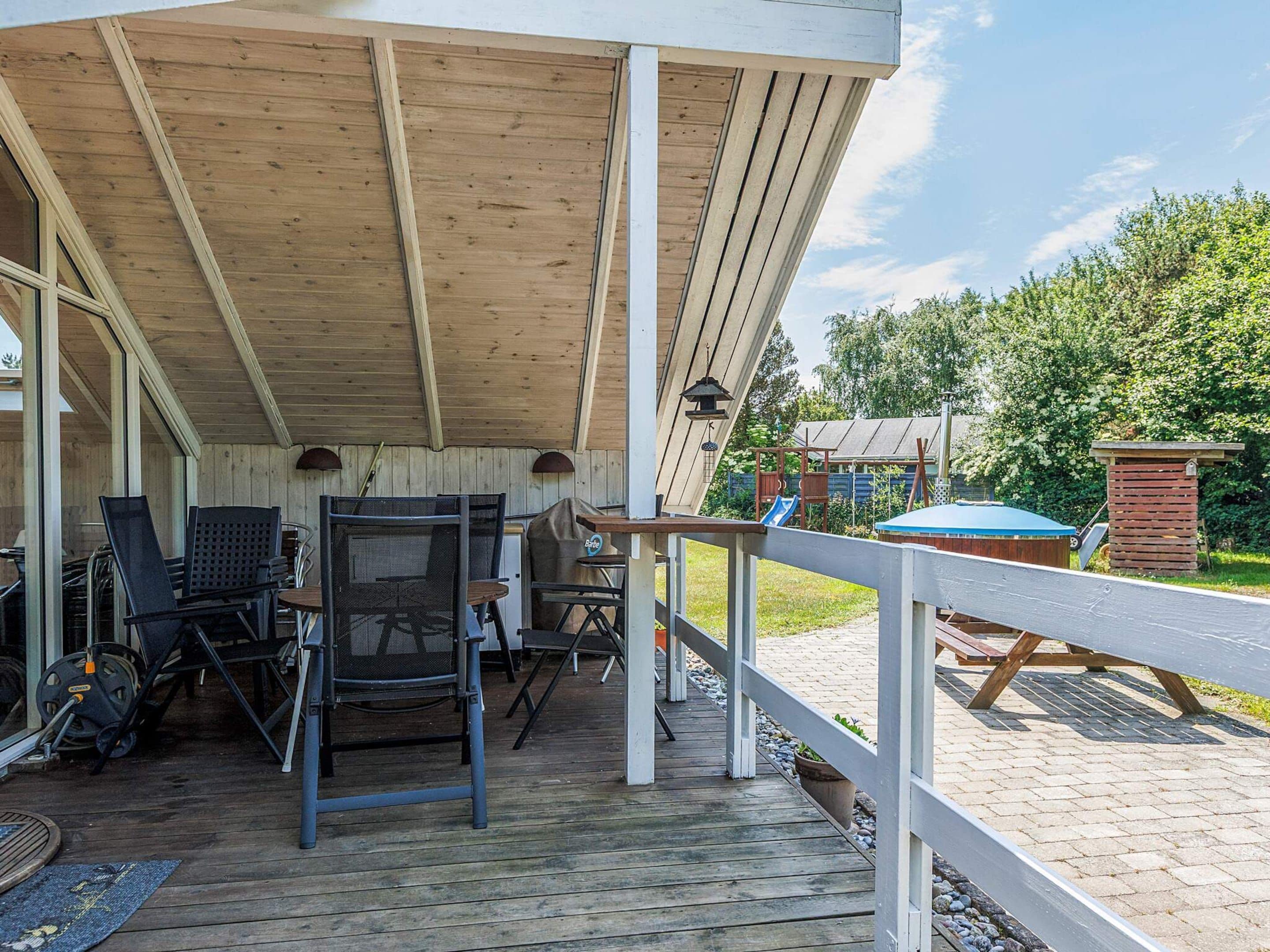 A covered outdoor patio with a wooden deck, metal chairs, and a barbecue grill.