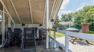A covered outdoor patio with a wooden deck, metal chairs, and a barbecue grill.