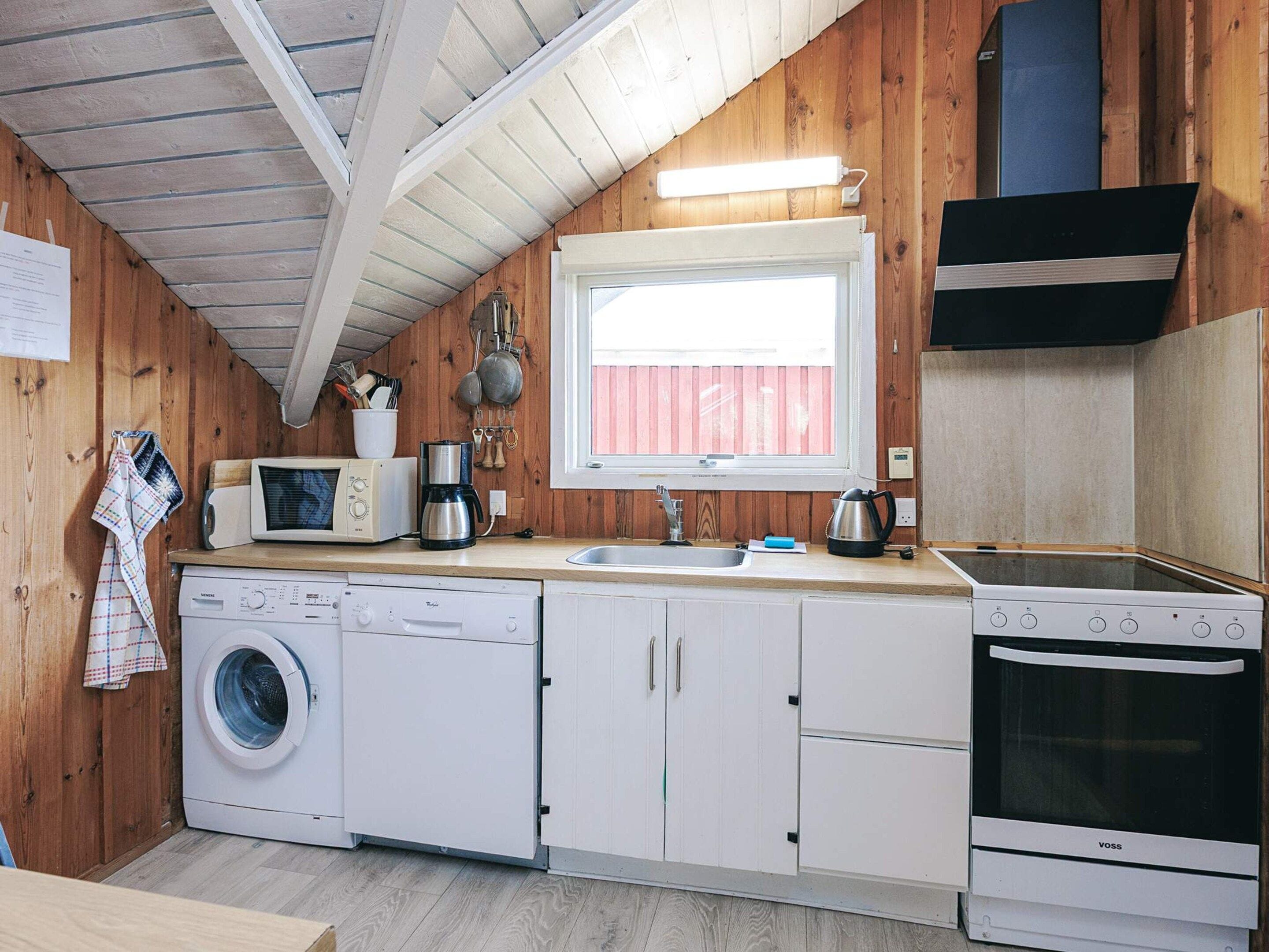 A compact kitchen with a washing machine, microwave, coffee maker, and stove.