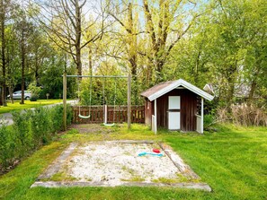 A small wooden shed with a sloped roof, a swing set, and a sandbox in a grassy area with trees in the background. - 8 Person Holiday Home in Hemmet (Hemmet)