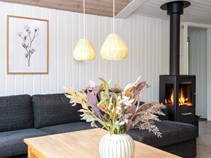 A modern living room with a sofa, a wooden coffee table, a vase with dried flowers, two hanging lamps, and a wood-burning stove. - 8 Person Holiday Home in Hemmet (Hemmet)