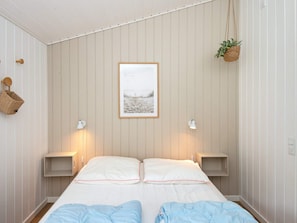Un dormitorio con dos camas, un cuadro enmarcado en la pared, lámparas de noche y una planta colgante.