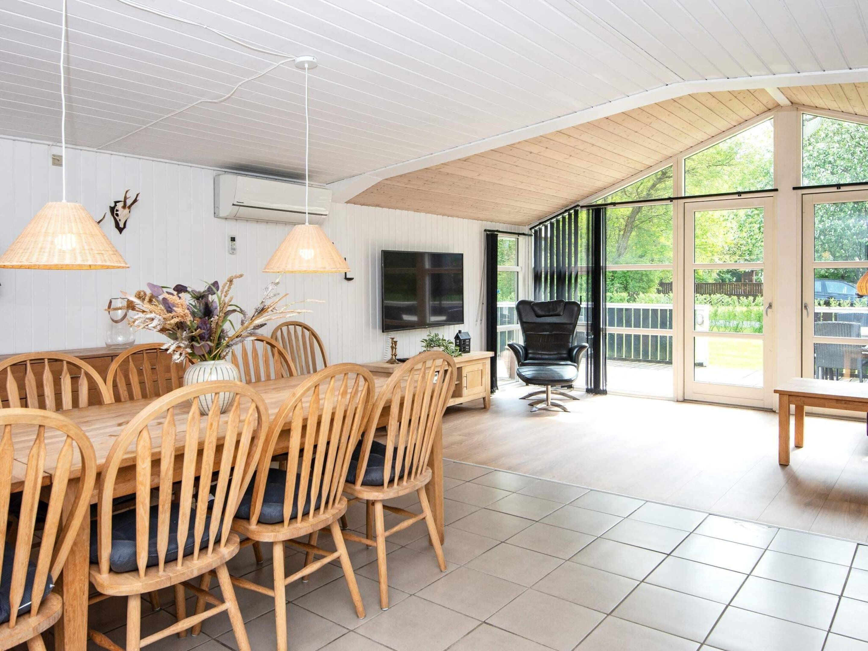 A dining area with a wooden table and chairs, a television, and a large window with a view of greenery.