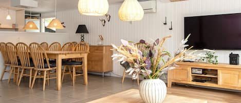 A modern living room with a wooden dining table, chairs, a large TV, and a decorative vase.
