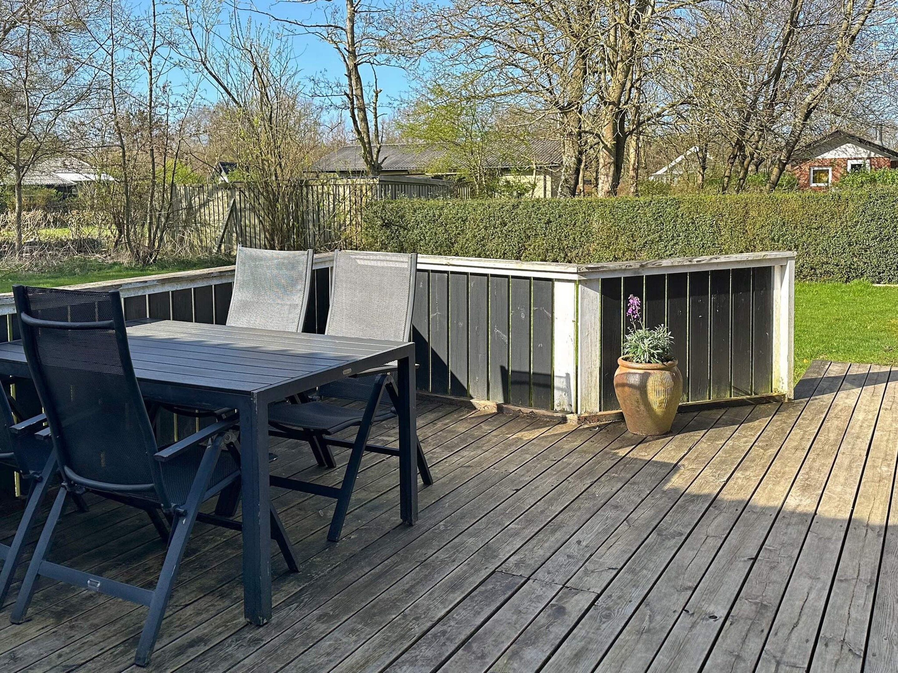 An outdoor deck with a table and chairs, surrounded by a wooden fence and a small shed.
