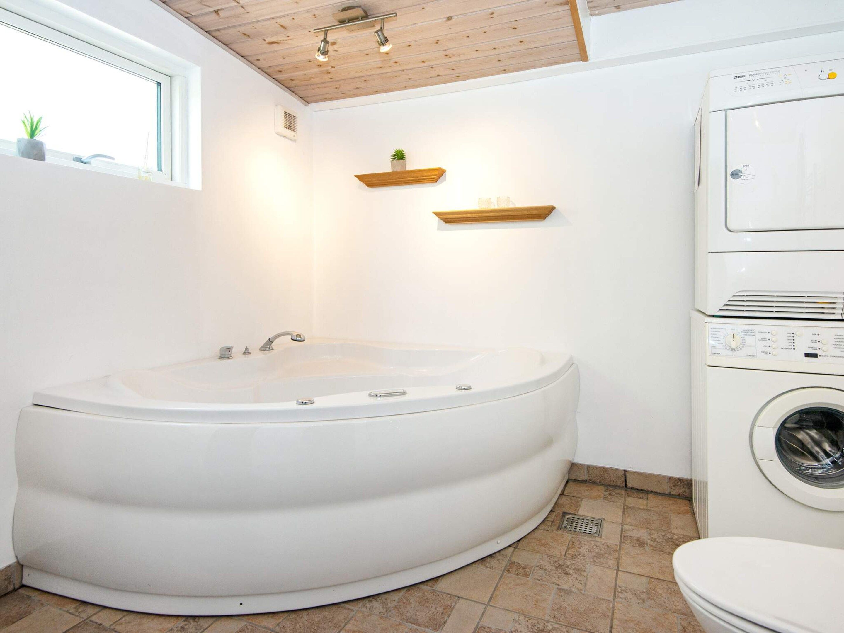 Une salle de bain avec une baignoire sur pieds, un lave-linge encastré et une fenêtre agrémentée de plantes.