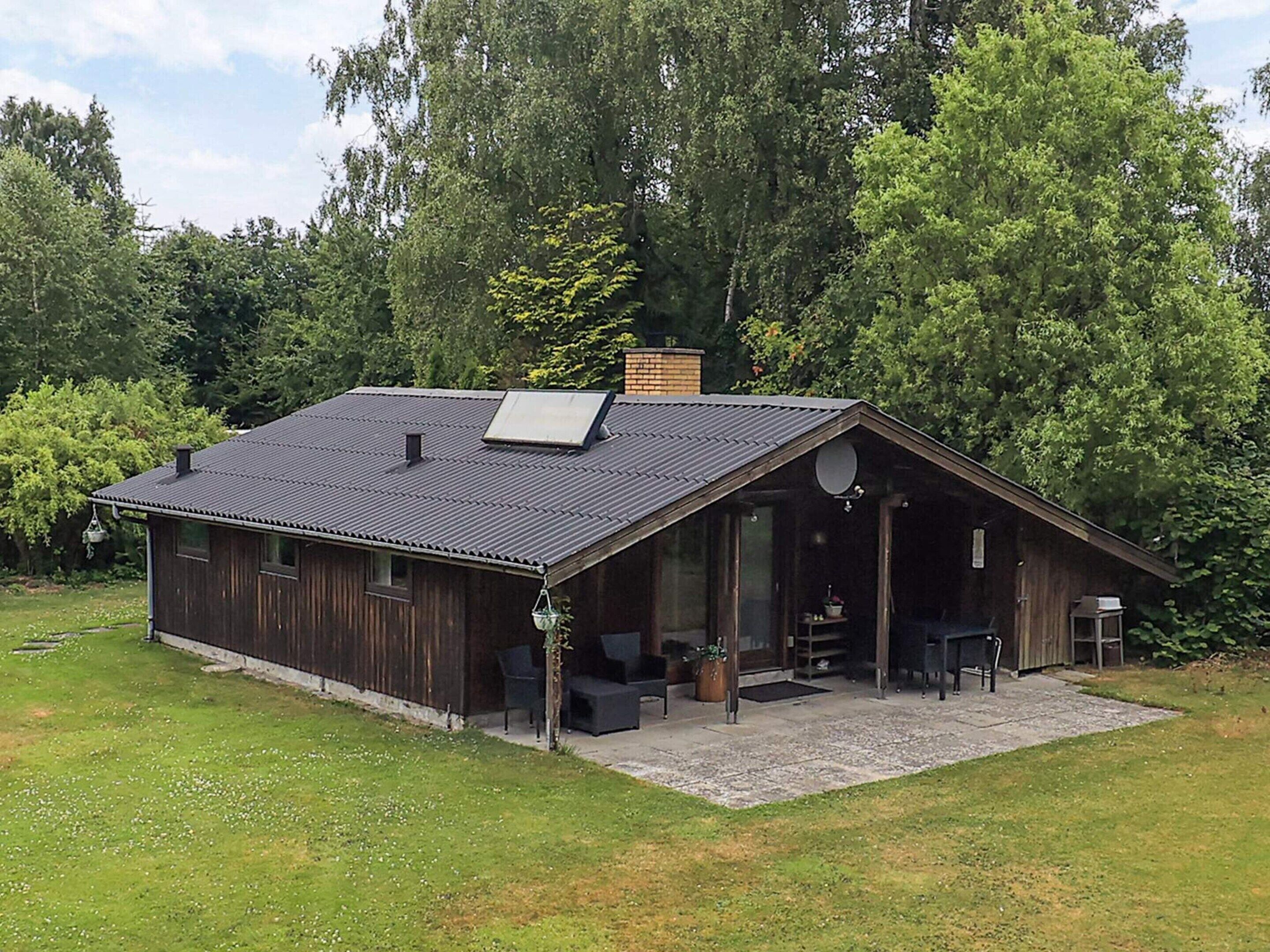 A rustic cabin with a large porch, a chimney, and a solar panel on the roof.