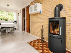 A modern interior with a wood-burning stove, a dining area with a white table and chairs, and a brick wall. - 4 Star Holiday Home in Idestrup (Idestrup)
