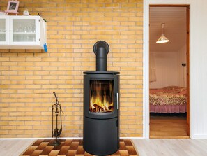 A room with a wood-burning stove, a white cabinet with glass doors, and a bed with a patterned bedspread. - 4 Star Holiday Home in Idestrup (Idestrup)