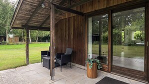 Ein überdachter Patio-Bereich mit Gartenmöbeln, einer Holzhütte und einer großen Schiebeglastür zum Garten.