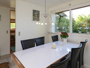 A dining area with a white table, black chairs, a vase with flowers, and a window with plants. - 4 Star Holiday Home in Idestrup (Idestrup)