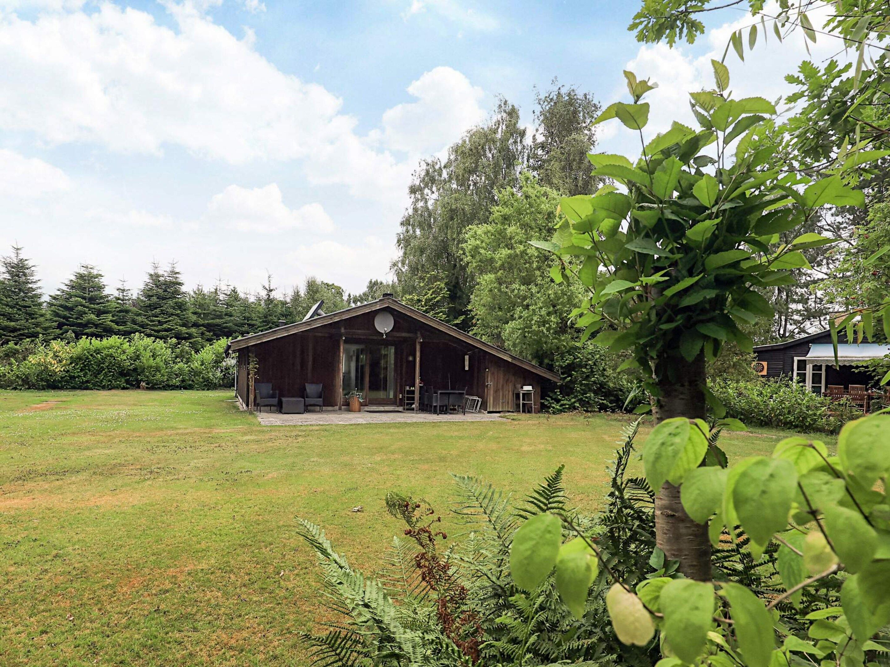 A wooden cabin with a covered porch, surrounded by a grassy yard and dense trees.