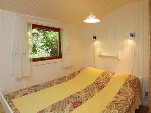 Ein Zimmer mit einem Bett, einem Vorhangfenster, einer Pendelleuchte und einem Wandregal.
