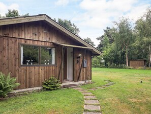 A wooden cabin with a porch, a window with potted plants, and a stone pathway leading to the entrance. - 4 Star Holiday Home in Idestrup (Idestrup)