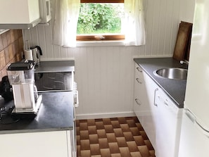 A compact kitchen with white cabinets, a built-in dishwasher, a sink, and a window with a view of greenery. - 4 Star Holiday Home in Idestrup (Idestrup)