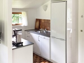 A compact kitchen with white cabinets, a stainless steel sink, and a built-in refrigerator. - 4 Star Holiday Home in Idestrup (Idestrup)