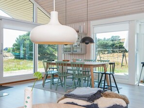 Ein moderner Essbereich mit einem Holztisch und Stühlen, einer Hängeleuchte und Blick ins Freie.