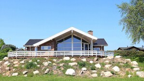 Une maison moderne dotée d’une grande baie vitrée, d’une terrasse blanche et de fondations en pierre.