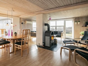 A modern living room with a wood-paneled ceiling, a fireplace, and a dining area with wooden furniture.