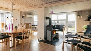 A modern living room with a wood-paneled ceiling, a fireplace, and a dining area with wooden furniture. - 4 Star Holiday Home in Lokken (Lokken)