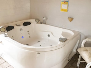 A white freestanding bathtub with a control panel, a small towel, and a wall-mounted light fixture.