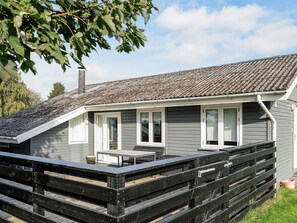 A single-story building with a sloped roof, a covered patio area with a table and chairs, and a wooden fence in the foreground. - Ideal Holiday Home in Stege near Sea (Stege)