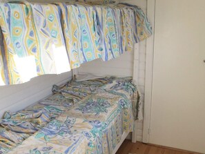 A single bed with a patterned bedspread in a room with white walls and a wooden floor. - Ideal Holiday Home in Stege near Sea (Stege)
