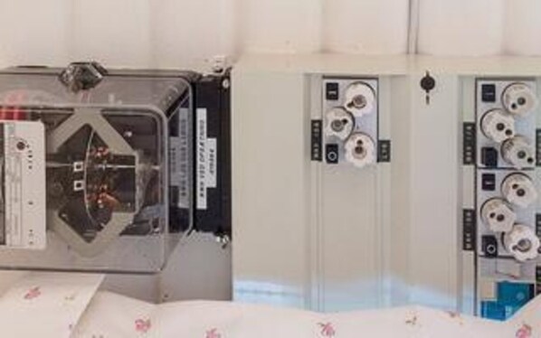 A room with a bed, a bedside table, and a wall-mounted control panel.