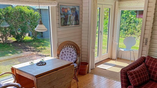 A cozy room with a wooden table, a wicker chair, a red plaid sofa, and a painting on the wall.