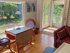 Una habitación acogedora con una mesa de madera, una silla de mimbre, un sofá rojo a cuadros y un cuadro en la pared.