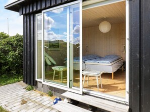 A modern cabin with a sliding glass door leading to a bedroom with a bed and a chair. - 4 Star Holiday Home in Ringkobing (Ringkobing)