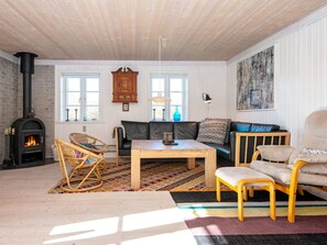 A cozy living room with a fireplace, a sofa, a coffee table, and a chair. - 4 Star Holiday Home in Ringkobing (Ringkobing)