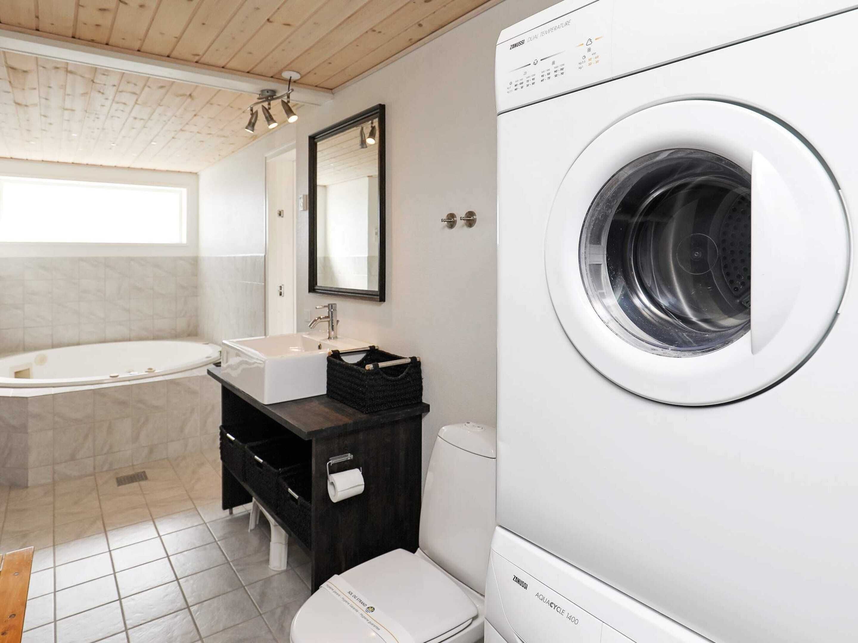 A modern bathroom with a bathtub, sink, mirror, toilet, and a front-loading washing machine.